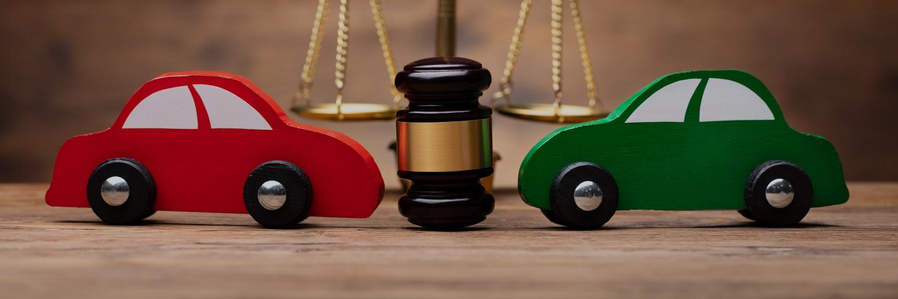 Which car Insurance is Mandatory in Ontario illustrated by two toy cars pointing toward a judge's gavel between them with scales in the background.