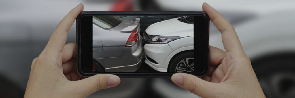 Someone taking a picture of a fender bender auto accident with a smartphone, being instructed what to do in a car accident.