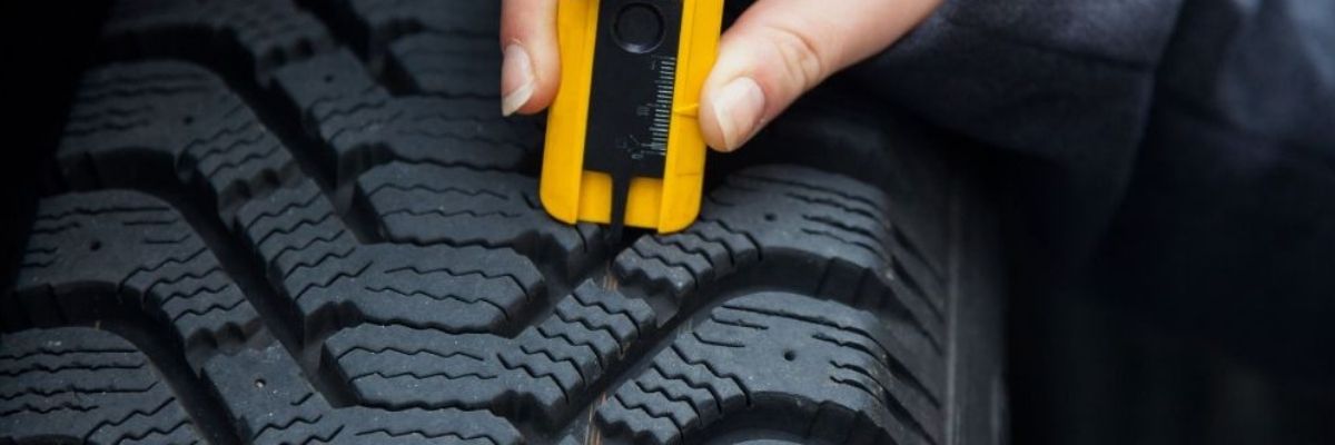 Hand checking tire tread on a used car with a special tool from the auto shop.