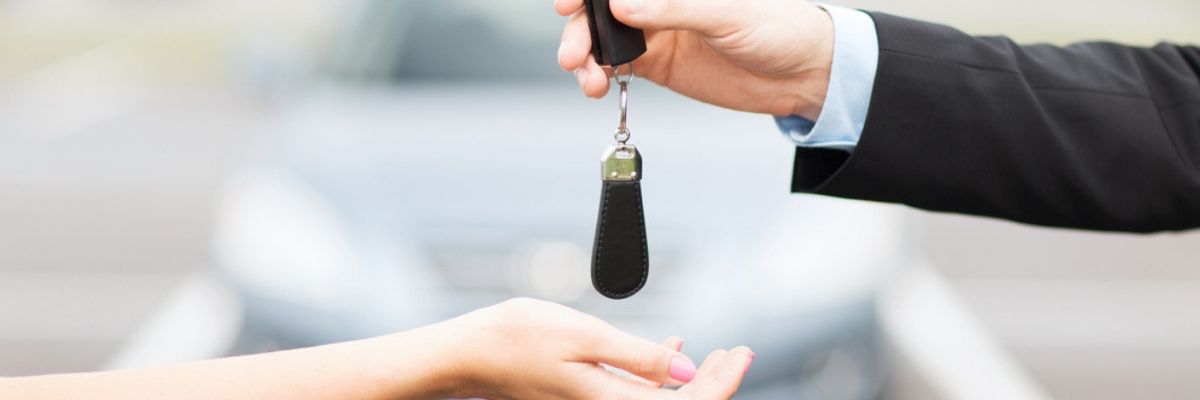 Man providing tips for buying a used car while dropping keys into a women's hand for a test drive.