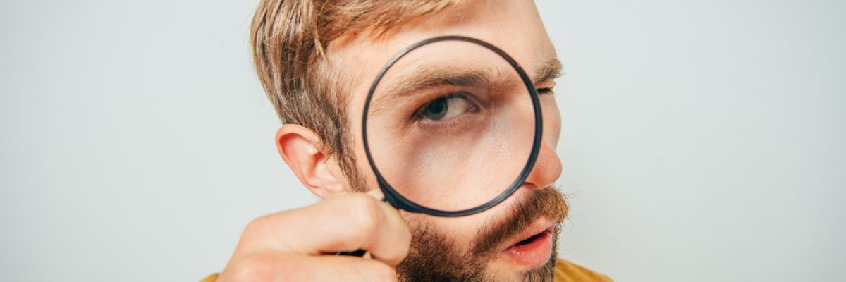 Blonde bearded man finding what to look for when buying a used car through a magnifying glass.