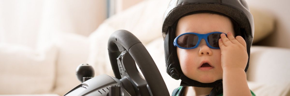 Baby wearing helmet and sunglasses behind a toy steering wheel, figuring out how to buy cars online safely.