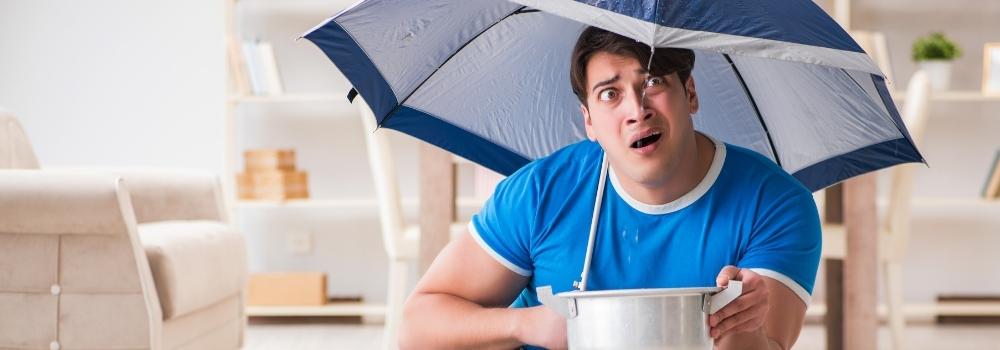 Man holding umbrella inside his home because he believed the home insurance myth that every policy has home flood coverage.