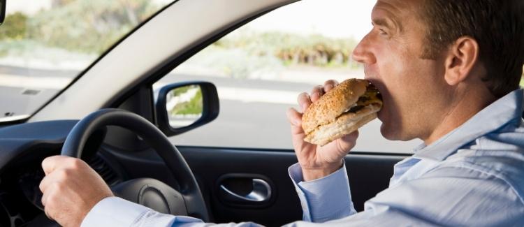 Middle-aged man eating a hamburger, committing careless driving in Ontario.