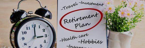 "Retirement plan" circled in red marker on a to-do list beside an old-fashioned alarm clock and a small pot of flowers.