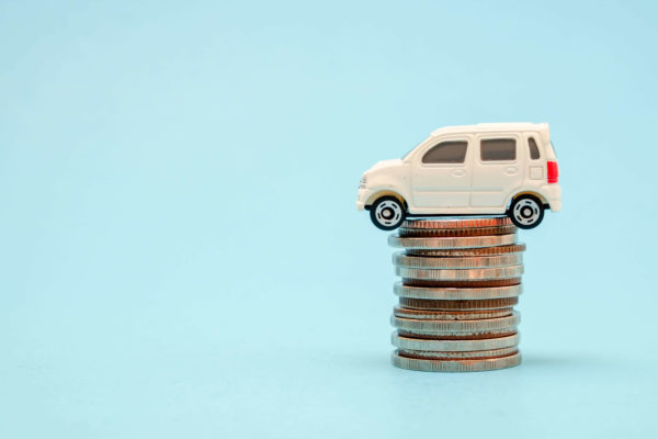 "Car insurance discounts in Ontario" Illustrated by a white toy car sitting on top of a stack of coins.