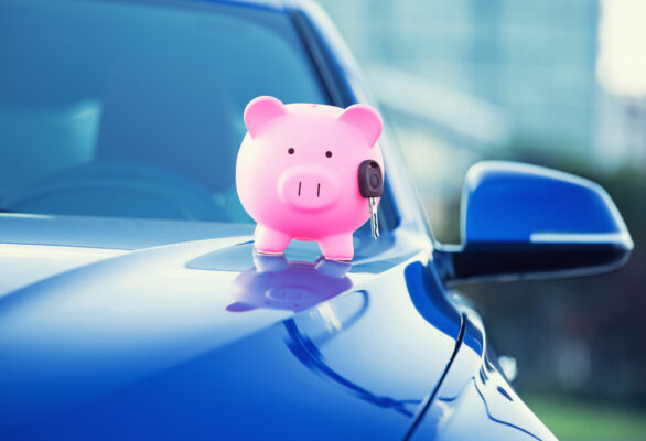a pink piggie bank holding keys ontop of a blue car representing the savings for how much car insurance decreases after a year
